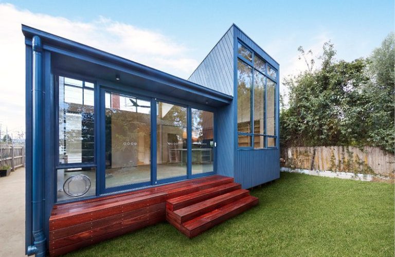 A blue shipping container home featuring a deck and steps, showcasing modern design and outdoor living space.